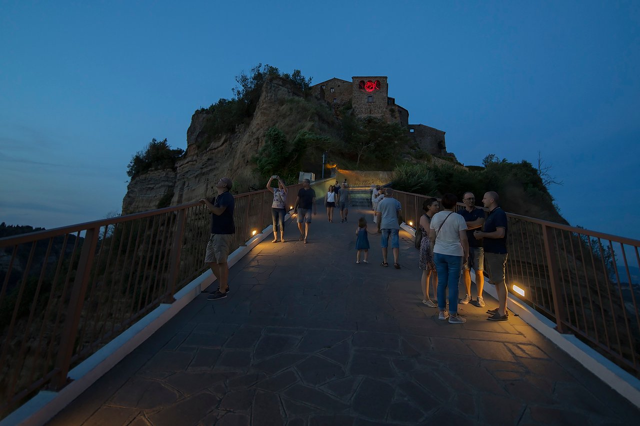 Grimanesa Amorós CETHA, 15 x 10 x 5-foot public art LED sculpture and light sculpture installed at the entrance of Civita di Bagnoregio, Palazzo Colesanti, Viterbo, Italy, 2019. Named after the Etruscan word for "sun," red and rose LED tubing blazes at the top of the town's steep pedestrian bridge, greeting and bidding farewell to every visitor, its dawn-colored light sequence honoring the ancient Etruscans who founded this UNESCO-recognized hilltop city. Light sculpture by Grimanesa Amorós.