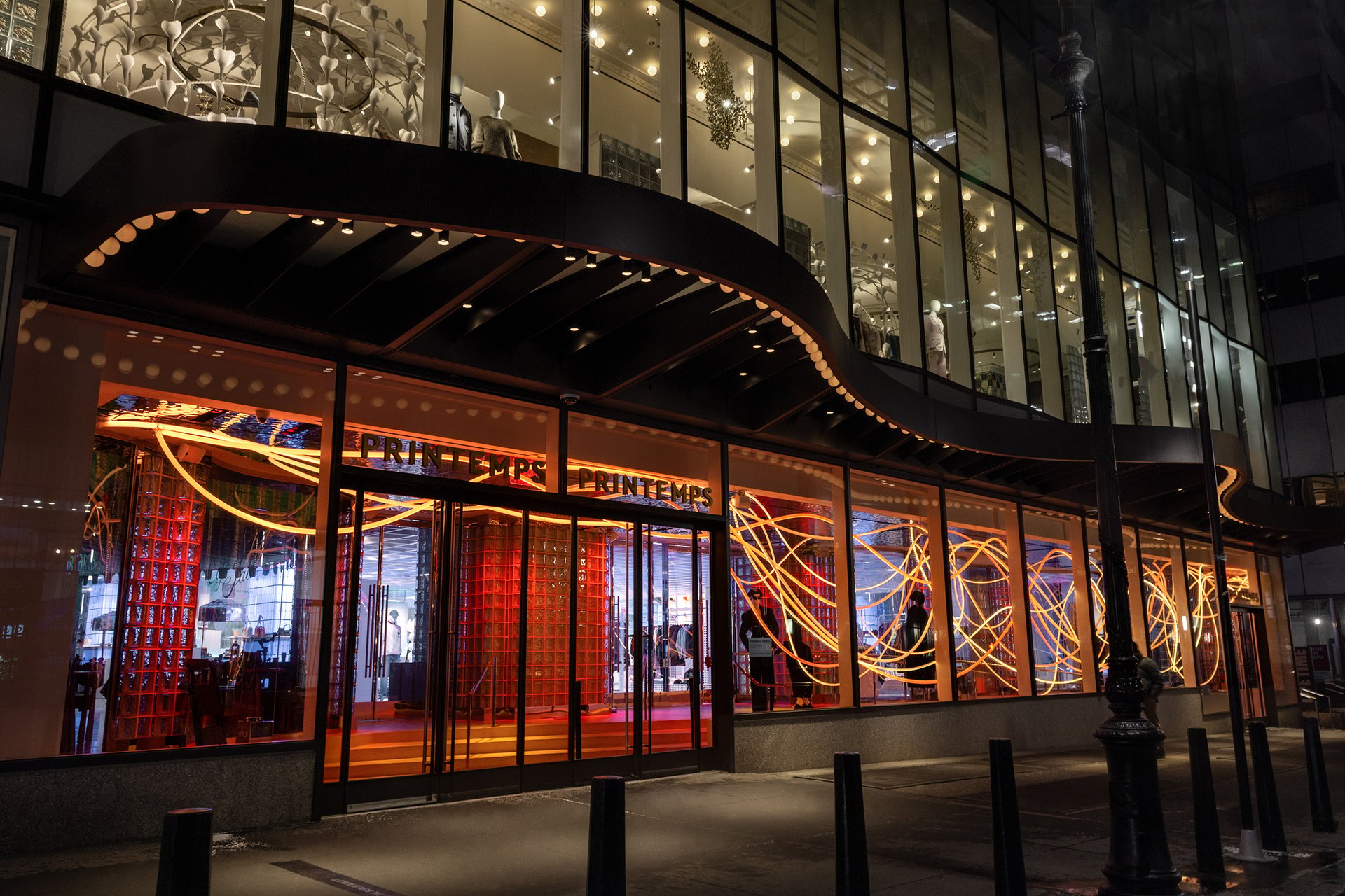 PERFECT TIMING, a site-specific light installation by Grimanesa Amorós on Wall Street, New York City, featuring suspended luminous sculptures that pulse and shift through warm golds, vibrant ambers, and subtle silvers, creating a rhythmic interplay of glowing light and shadow across the architectural space, evoking the flow of time and the energy of the urban environment in an immersive, radiant experience.