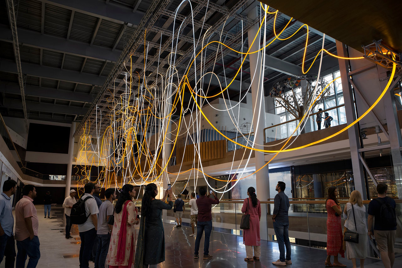Monumental light installation Golden Array by light artist Grimanesa Amorós, spanning 210 feet by 25 feet by 70 feet. Inspired by India's cable lines, it features a dynamic sequence of golden yellow, warm orange, and bright white lights that flow rhythmically, reminding the viewer of the profound web that binds humanity.