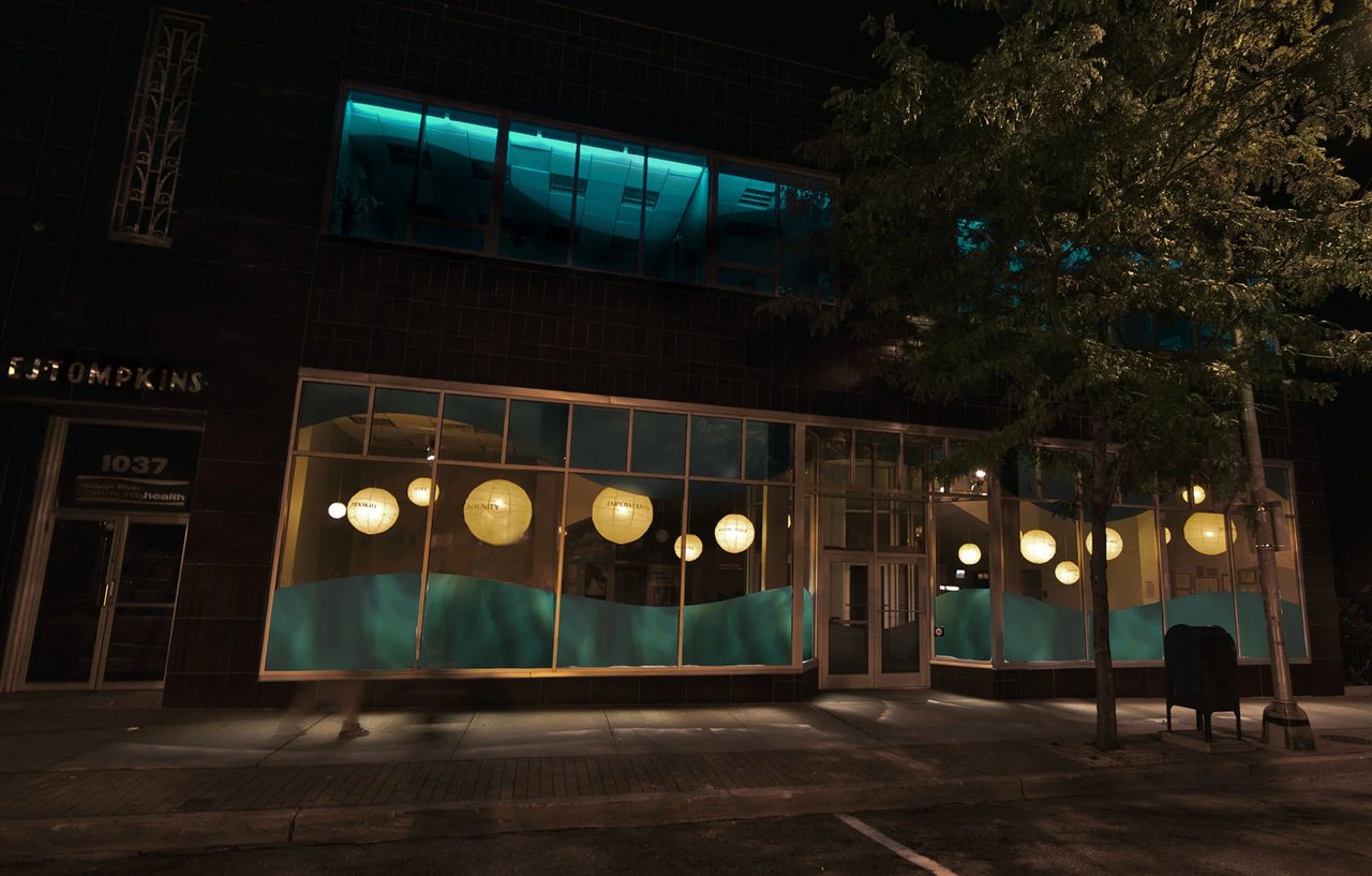 Grimanesa Amorós SUBSTANCIAL, permanent 33 x 55 x 12-foot public art light sculpture and LED art on the facade of Sun River Health, formerly HRHCare, Peekskill, New York, 2005 to 2007. Acrylic convex-lens LED glowing paper lanterns bearing bilingual words honoring the four founding women of HRHCare flow through a visual river of water-like plastic sheeting, illuminating the health center's community mission in light and color. Light sculpture by Grimanesa Amorós.