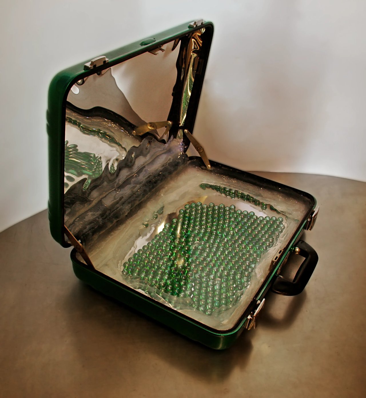Grimanesa Amorós REMOLINO, sculpture measuring 14 x 18 x 4.5 inches closed and 14 x 18 x 16 inches open, a mirrored suitcase containing marbles representing the dreams, memes, and schemes we carry when moving to a new place, its reflective interior mirroring the viewer as a meditation on identity and belonging. Exhibited as part of the Optica Festival 2009, traveling to Bolivia, Argentina, Spain, and beyond, and shown alongside REMOLINO at the Tina B. Festival, Prague, Czech Republic.