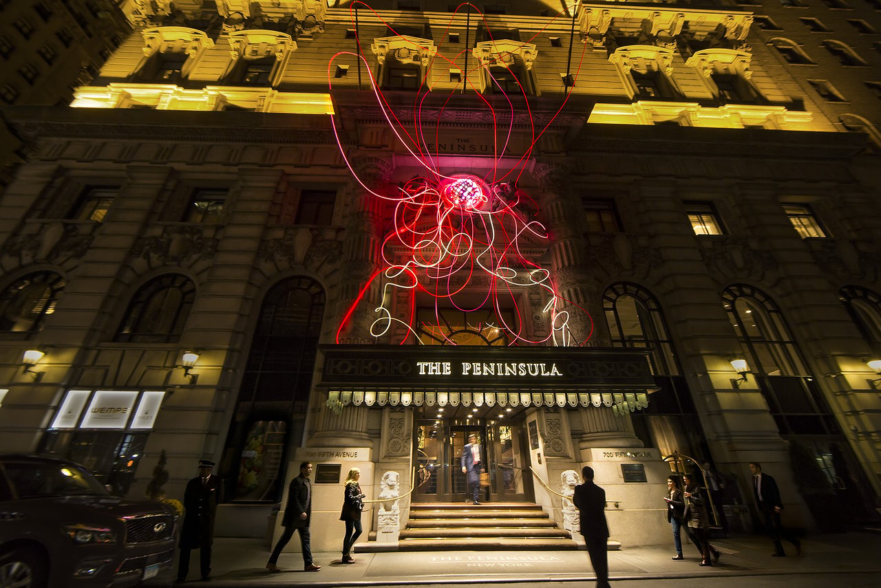 Grimanesa Amorós PINK LOTUS, 41 x 31 x 17-foot public art light sculpture and LED sculpture on the landmarked Beaux-Arts facade of The Peninsula Hotel New York, Fifth Avenue, 2015. A glowing pink LED lotus made of diffusion and reflective material, and LEDs, positioned between the carved Roman goddesses Ceres and Diana, created for The Art of Pink Breast Cancer Awareness Month initiative. Light sculpture by Grimanesa Amorós.